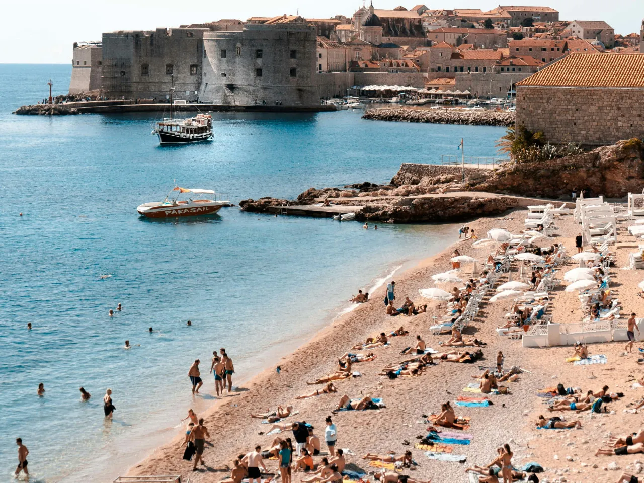 Banje beach with swimmers and sunbathers, and Dubrovnik Old Town and Fort St John behind